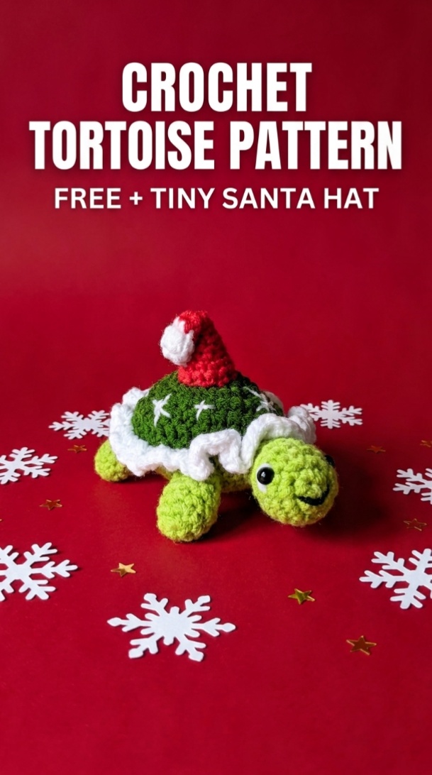 Crocheted green tortoise wearing a red Santa hat with a white ruffled edge around its dark green shell
