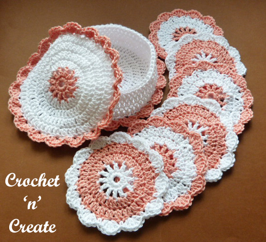 Set of white and dusty pink crocheted round coasters with scalloped edges fanned out beside a matching lidded crocheted basket to store them in