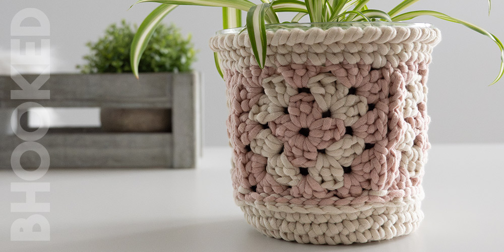 Pink and cream granny square crochet plant pot cover on a pot holding a spider plant