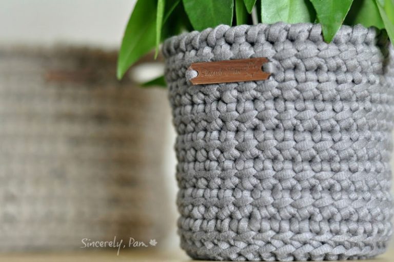 Grey crochet plant pot cover in dense linked double crochet with a small leather tag, holding a leafy plant