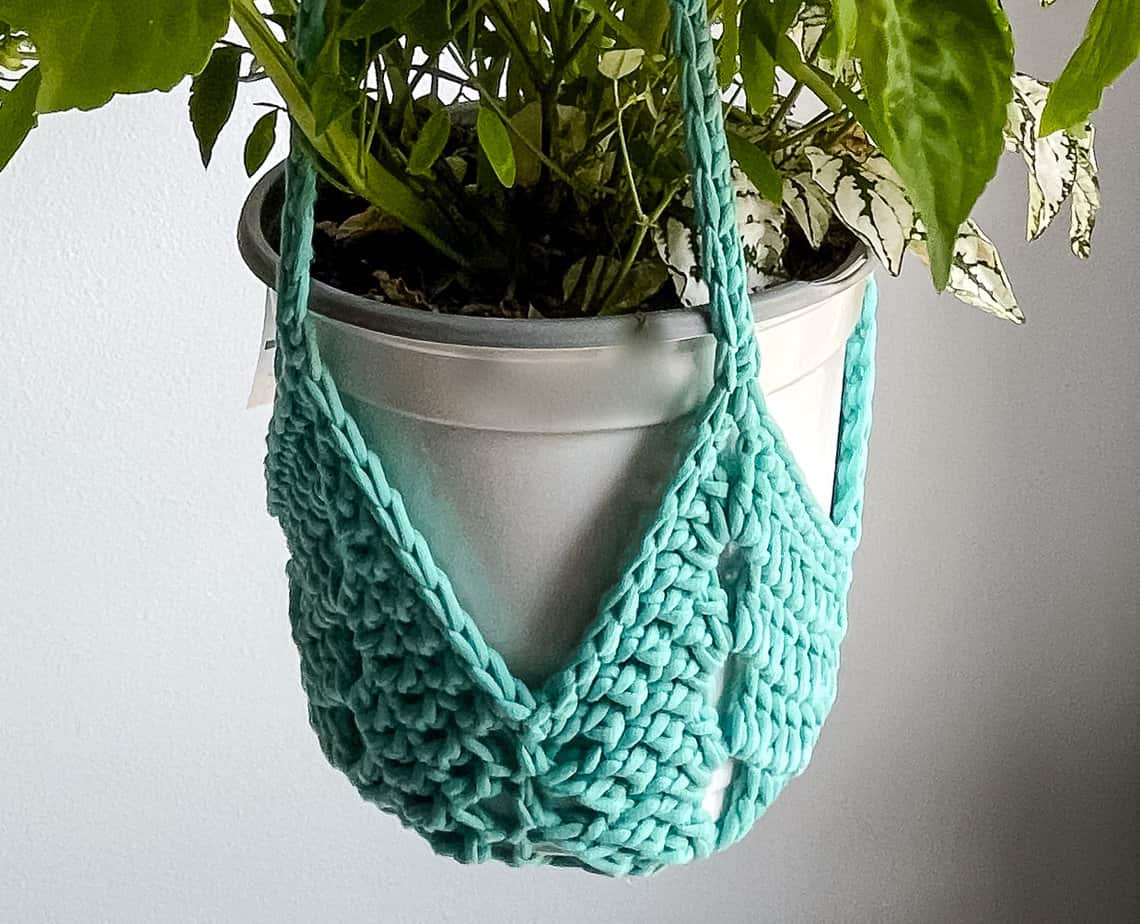 Teal never ending star crochet plant hanger holding a white plastic pot with a leafy plant