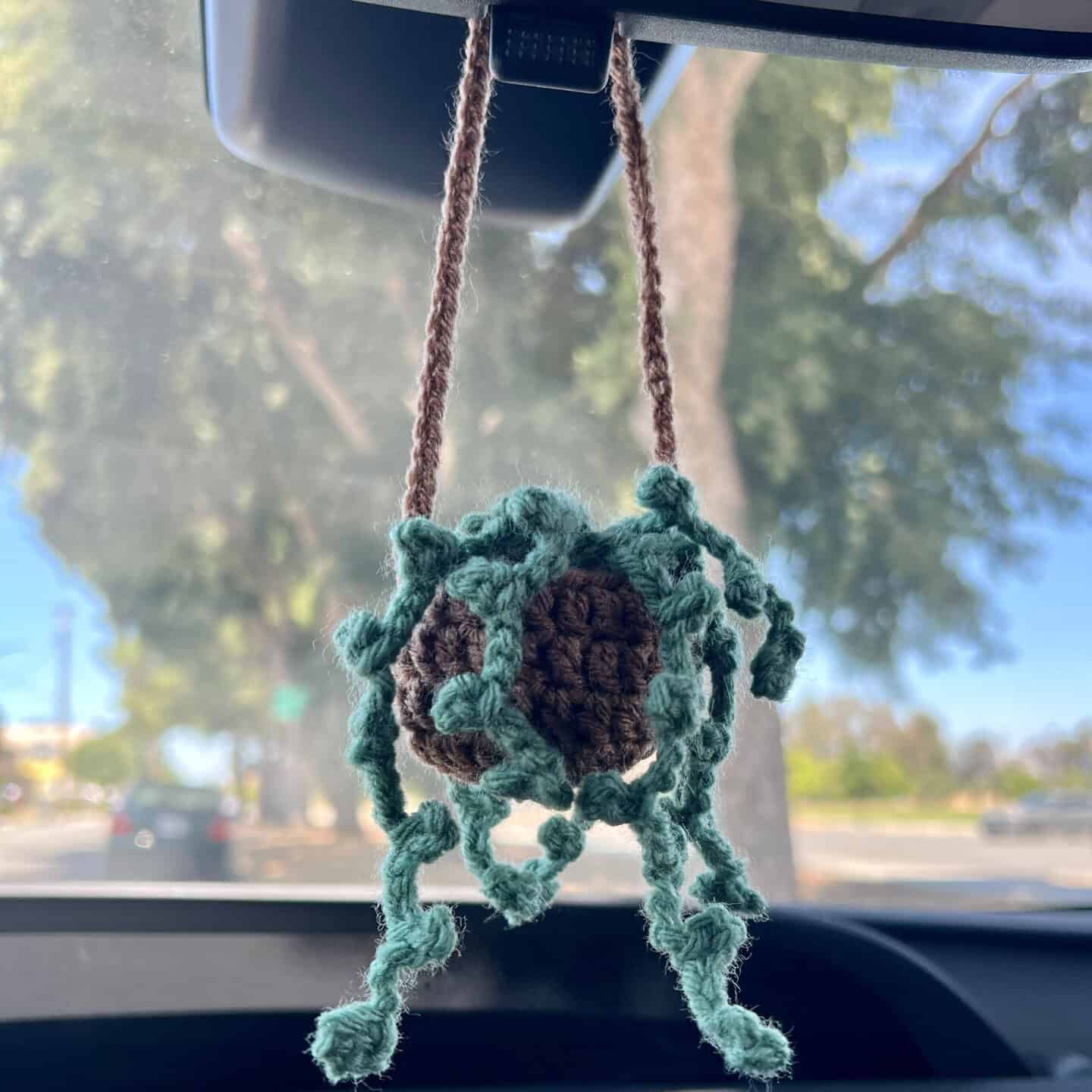 Crocheted string of pearls car hanging plant in a brown pot dangling from a rearview mirror