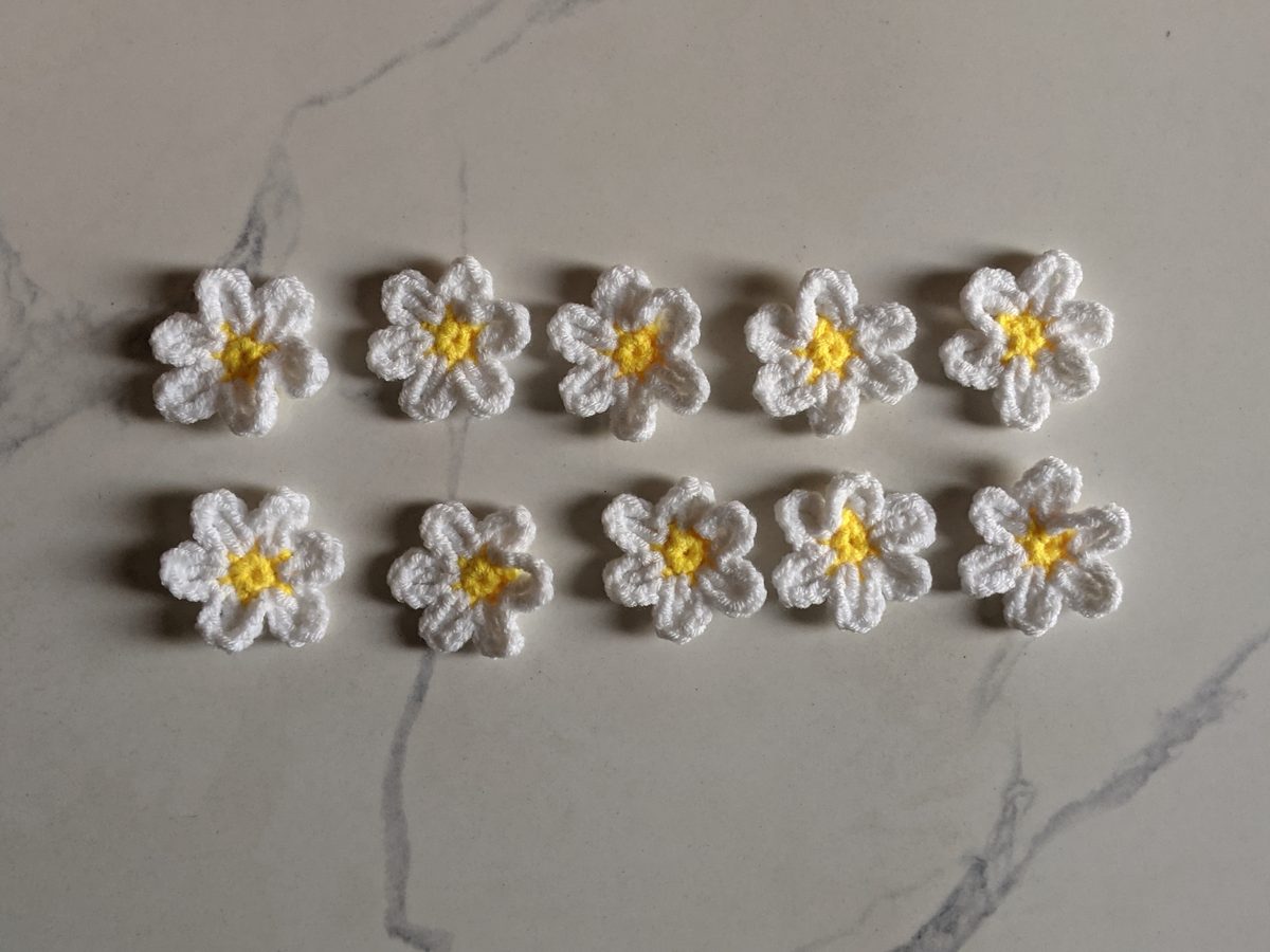 Ten finished white crochet daisies with yellow centers laid out in two rows on marble