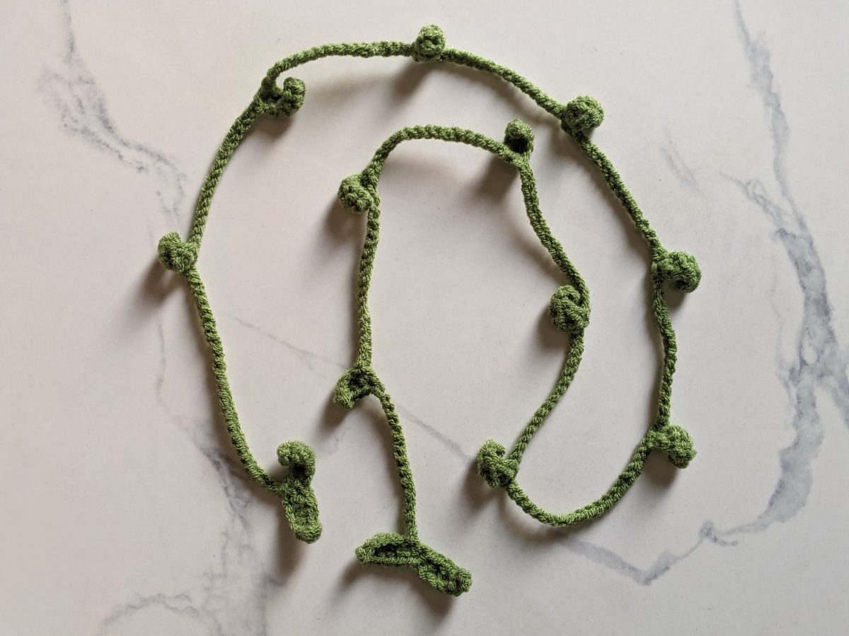 The finished green crochet leaf vine with small leaves along its length, laid in loops on marble before the flowers are added