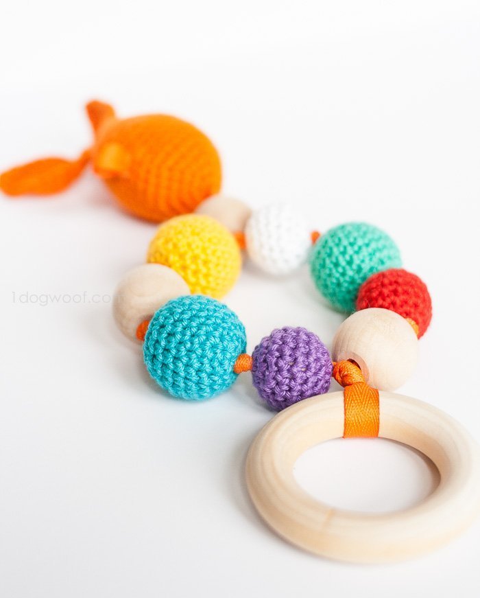 Crochet baby teether with an orange goldfish at the top, a row of colorful crocheted beads and a wooden teething ring